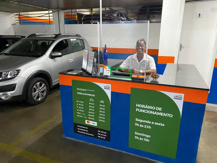 Atendente na cabine de uma unidade Atlas Park, com quadro de horário de funcionamento